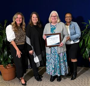 Four women standing together, one is receiving a reward.