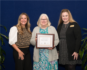 Three women standing together, one is receiving a reward.